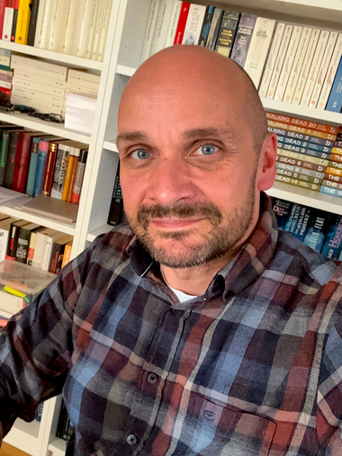 Das Foto zeigt unseren Autoren Henry Cardell vor seinem Bücherregal